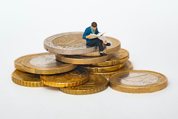 A model of a man reading a paper sits on a pile of coins Merchant Cash Advances