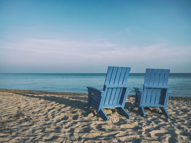 Two blue deck chairs on the beach looking out to a blue sky. 