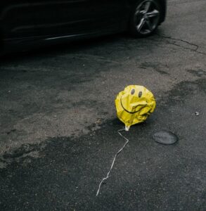 A deflated balloon with a smiling face lies on the road uncertainty