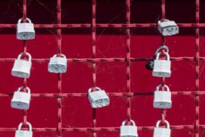 Metal padlocks hang on a red chainlink french.  Alternative Investments