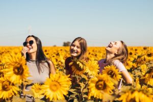 Three women laughing and smiling in a sunflower field Misery Index