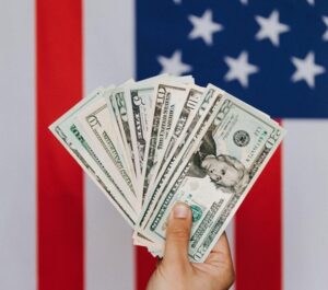 Hand holding a spread of fiat currency with US flag background for ‘Bank of America's CEO Predicts Economic Soft Landing: What It Means for You’