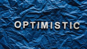 The word ‘optimistic’ spelled out on blue paper ‘2024 Outlook: Steering the US Economy to Stability’