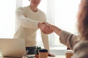 Two people shaking hands over a desk for ‘2024 Outlook- Steering the US Economy to Stability’