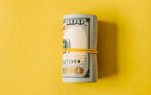 A roll of hundred dollar bills against a yellow background for ‘Federal Reserve Update - What Investors Need to Know’