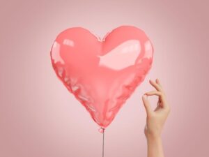Digital rendering of pink balloon with hand holding a pin next to it for ‘Understanding The New Buzzword for Today’s Economy- Deflation’ deflation