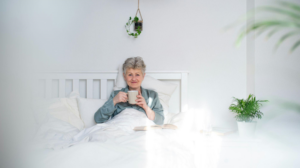 Interior, a smiling elderly woman sits in bed whilst sipping tea, for “How to Build a Portfolio for a Long Retirement”
