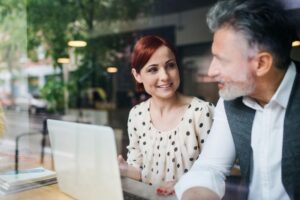 Interior, two people chat in a cafe over a laptop, for “The Best Risk Management Strategies for Family Offices”